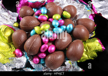 Pile d'oeufs de pâques en chocolat emballé avec le papier aluminium rétractable qui l'entourent sur un fond noir. Banque D'Images