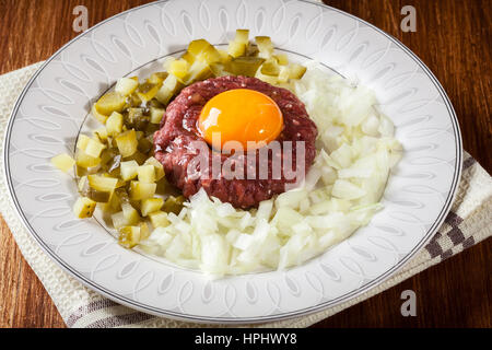 Steak tartare avec le jaune d'œuf, les oignons et les cornichons sur une plaque Banque D'Images