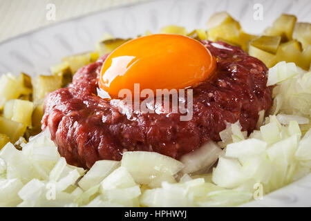 Steak tartare avec le jaune d'œuf, les oignons et les cornichons sur une plaque Banque D'Images