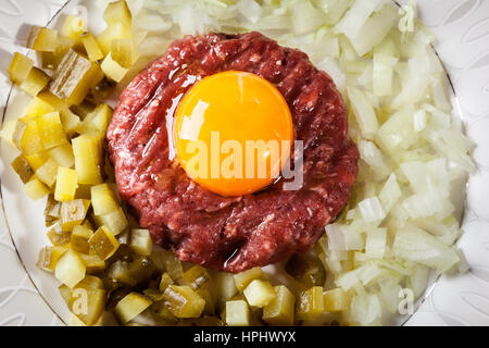 Steak tartare avec le jaune d'œuf, les oignons et les cornichons sur une plaque Banque D'Images