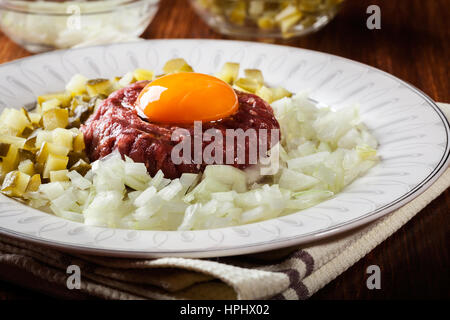 Steak tartare avec le jaune d'œuf, les oignons et les cornichons sur une plaque Banque D'Images