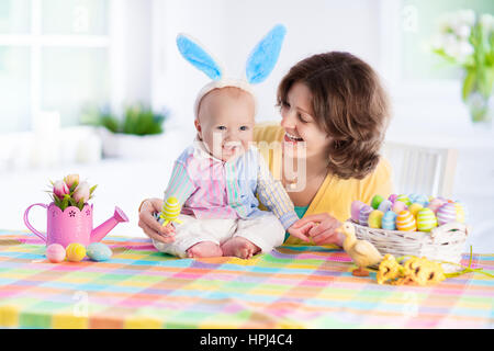 La mère et l'enfant les oeufs colorés de peinture. Maman et bébé avec oreilles de lapin peindre et décorer des oeufs de Pâques. Parent et enfant jouer à l'intérieur au printemps. Décorées Banque D'Images