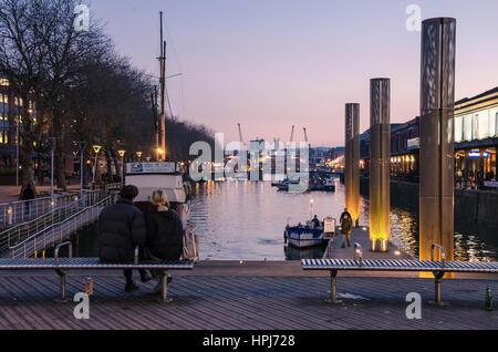 Un couple s'asseoir dehors sur un banc avec vue sur le port de Bristol juste après le coucher du soleil en début de soirée et profiter de la vue. Banque D'Images