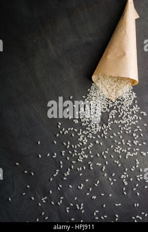 Riz blanc éparpillés sur la table en bois sombre d'un sac en papier. Vue de dessus. L'espace pour le texte. Banque D'Images