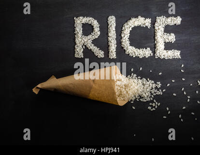 Riz blanc éparpillés sur la table en bois sombre d'un sac en papier. Vue de dessus. L'espace pour le texte. Banque D'Images