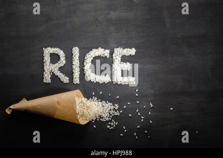 Riz blanc éparpillés sur la table en bois sombre d'un sac en papier. Vue de dessus. L'espace pour le texte. Banque D'Images