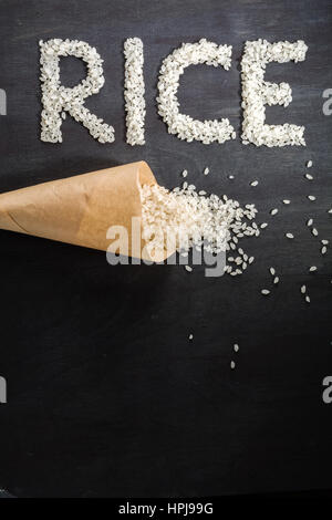 Riz blanc éparpillés sur la table en bois sombre d'un sac en papier. Vue de dessus. L'espace pour le texte. Banque D'Images