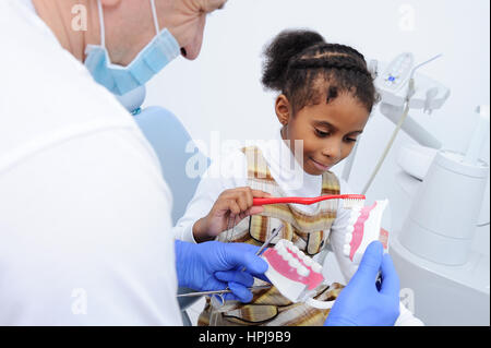 Dentiste pédiatrique montre homme fille africaine avec la peau foncée comment bien brosser les dents sur un modèle de la mâchoire Banque D'Images