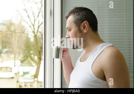 Tôt le matin, l'homme de boire du café et regarder par la fenêtre Banque D'Images