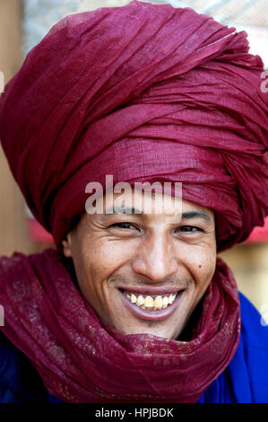 Portrait d'un Bédouin nomad avec turban écarlate et grand sourire de vendre ses marchandises dans populaires site du patrimoine mondial de Ait Benhaddou, Maroc. Banque D'Images