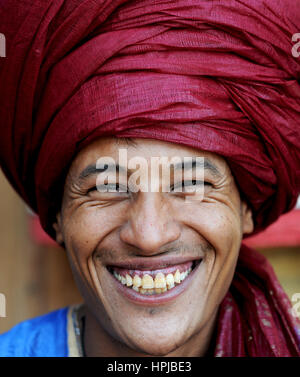 Portrait d'un Bédouin nomad avec turban écarlate et grand sourire de vendre ses marchandises dans populaires site du patrimoine mondial de Ait Benhaddou au Maroc. Banque D'Images