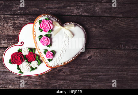 Les cookies en forme de coeur avec des roses glaçage sur fond de bois rustique. Pour dessert romantique femme aimée. Banque D'Images