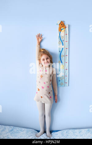 Petite fille blonde hauteur de mesure contre le mur dans la pièce Banque D'Images