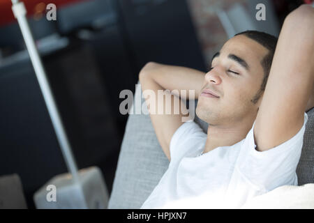 Jeune homme avec ses yeux fermés et ses bras croisés derrière sa tête, parce qu'il est détendu de penser ou de rêver de quelque chose de très agréable, il est en Banque D'Images