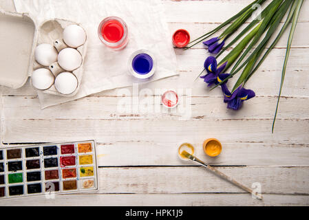 Vue de dessus les oeufs de poule en boîte avec les peintures et iris fleurs sur table en bois Banque D'Images