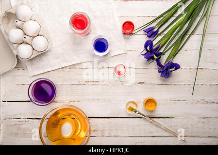 Vue de dessus les oeufs de poule en boîte avec les peintures et iris fleurs sur table en bois Banque D'Images