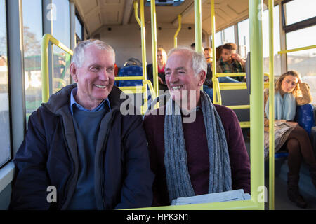 Deux hommes sourire et parler sur le bus. Il y a d'autres gens assis sur le bus à l'arrière-plan. Banque D'Images