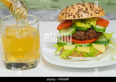 Grand Burger et la bière est versé dans un verre de près. Banque D'Images