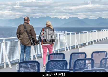 Un couple, seul sur le pont d'un ferry, tenir la main et de regarder à travers le détroit de Georgia à l'île de Bowen, Howe Sound et la côte de la Colombie-Britannique. Banque D'Images