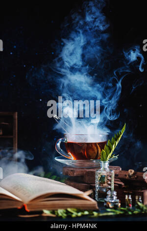 Une tasse de thé avec un bain à vapeur, un livre ouvert, des bouteilles en verre et les herbes sur fond sombre Banque D'Images