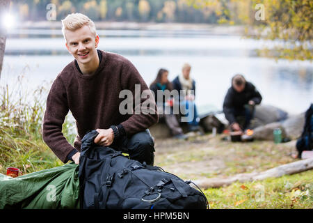 Portrait de jeune homme déballage de sac à dos avec les amis en arrière-plan de camping Banque D'Images