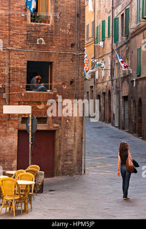 Homme assis dans la fenêtre à l'aide d'un téléphone mobile et jeune femme marche dans la rue , Siena, Toscane, Italie Banque D'Images