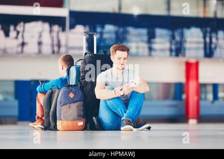 Deux amis voyageant ensemble. Voyageurs avec des téléphones mobiles en attente à l'aéroport, zone de départ de leur vol pour retard. Banque D'Images
