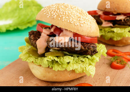 Escalope de foie avec des hamburgers, des tomates, des cornichons, de la laitue, sauce épicée et un pain avec des graines de sésame sur une planche à découper. Close up Banque D'Images