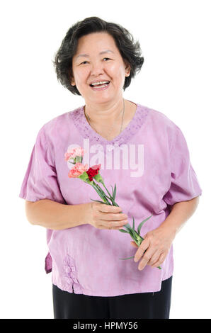 Happy mothers day concept. Portrait des années 60 Asian senior adult woman holding fleur oeillet cadeau et souriant, isolé sur fond blanc. Banque D'Images