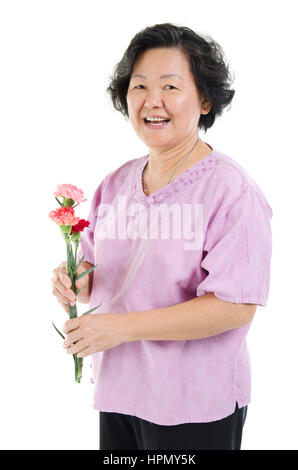 Happy mothers day concept. 1960 Asian senior adult woman holding fleur oeillet cadeau et souriant, isolé sur fond blanc. Banque D'Images