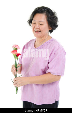 Heureux de célébrer la fête des mères, concept. Portrait des années 60 Asian senior adult woman holding fleur oeillet cadeau et souriant, isolé sur blanc retour Banque D'Images