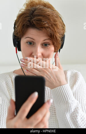 Femme dans un des écouteurs avec surprise attend at smartphone Banque D'Images