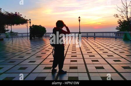 Silhouette d'une femme asiatique cheveux bouclés court article de prendre la photo de paysage spectaculaire lever du soleil avec l'appareil photo au point de vue balcon de Wat Phra Tha Banque D'Images