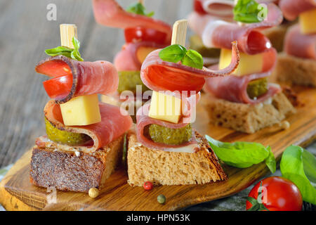 Apéritifs du Tyrol du Sud : pain de campagne frais beurré avec le lard fumé, fromage de montagne copieux, les cornichons et les tomates, les feuilles de basilic sur le dessus Banque D'Images