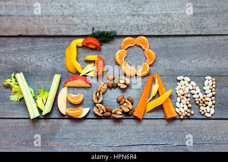 Mots 'Go vegan" écrit avec légumes, fruits, noix et légumineuses sur fond de bois rustique, concept - ingrédients biologiques pour une alimentation végétalienne saine Banque D'Images