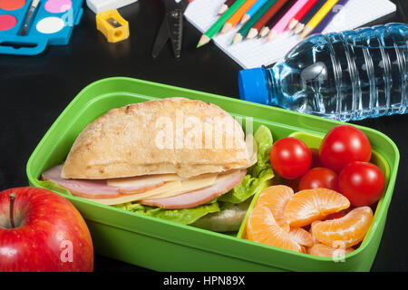 Déjeuner à l'école. Sandwich, petites tomates, la mandarine, l'apple en plastique boîte à lunch et une bouteille d'eau sur le tableau noir. Banque D'Images