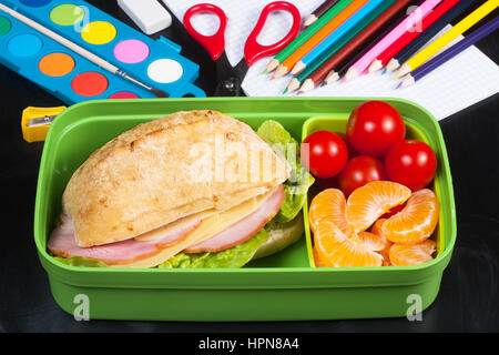 Déjeuner à l'école. Sandwich, petites tomates, la mandarine en boîte à lunch en plastique noir sur le tableau. Banque D'Images