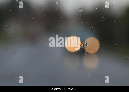 Phares des véhicules venant en sens inverse vu à travers la pluie sur un pare-brise Banque D'Images