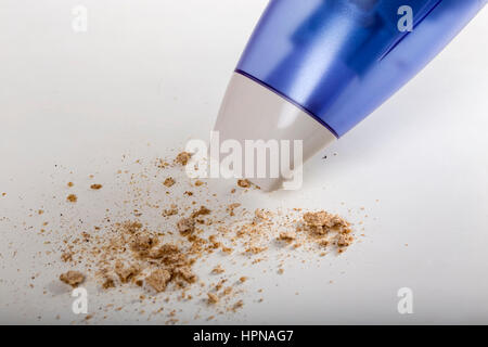 Aspirateur à main avec des miettes sur la surface de table blanc Banque D'Images