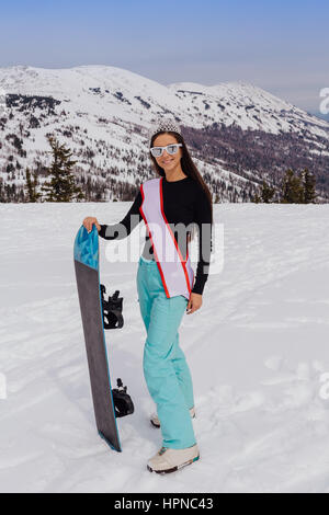 Belle fille de snowboard avec une couronne sur la tête debout sur le sommet de la montagne holding snowboard. Reine des neiges. Gagnant d'une beauté contes Banque D'Images