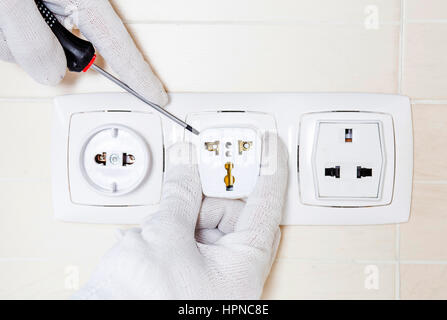 Electrician repairing socket avec un tournevis. Dans les mains des gants blancs. Banque D'Images