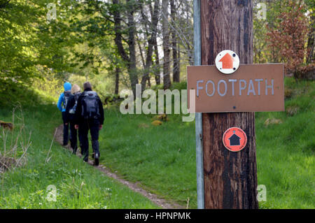 Trois randonneurs marche sur sentier par un post en bois avec Waymarker pour le Moyen-Orient Highland Way dans les Highlands, Ecosse, Royaume-Uni. Banque D'Images