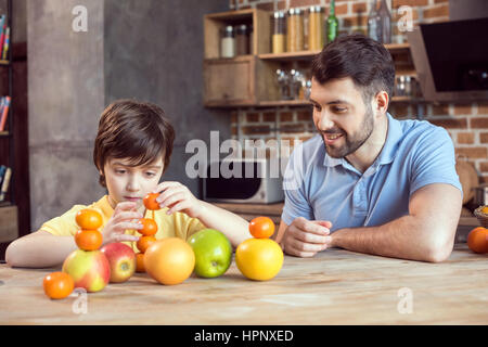 Père et fils jouant avec les agrumes à table de cuisine Banque D'Images
