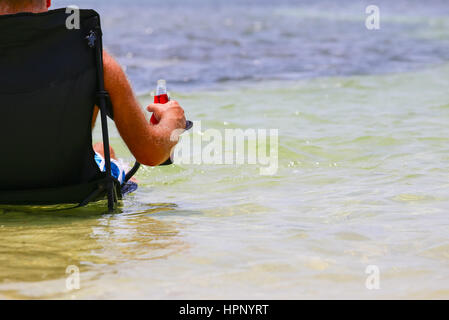 Big Pine Key, États-Unis - 10 mai 2015 : l'homme assis sur une chaise de camping dans les eaux peu profondes, près de la plage de Little Duck Key en Floride en prenant un verre. Banque D'Images