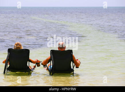 Big Pine Key, États-Unis - 10 mai 2015 : un couple assis sur des chaises de camping avec un verre dans l'eau peu profonde près de la plage de Little Duck Key en Floride. Banque D'Images