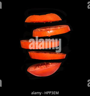 Flying tomato. Tranches de tomate rouge isolé sur fond noir. La légèreté des légumes flottant dans l'air. Banque D'Images
