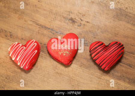 Macarons aux fraises en forme de coeur décorés de chocolat et d'or pour la Saint-Valentin, sur une surface en bois Banque D'Images