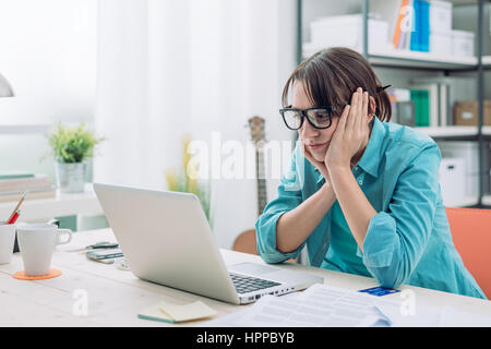 Jeune femme s'ennuie dans le bureau avec un ordinateur portable et à regarder l'écran d'ordinateur Banque D'Images