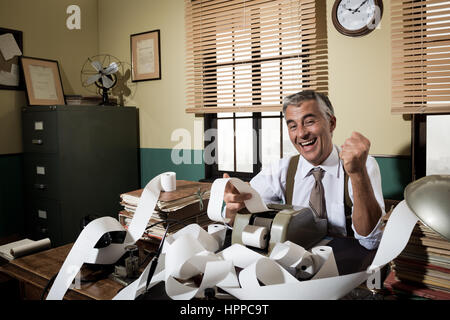 Cheerful vintage comptable entouré par l'ajout d'une bande de papier de la machine dans son bureau. Banque D'Images