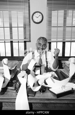 Cheerful vintage comptable entouré par l'ajout d'une bande de papier de la machine dans son bureau. Banque D'Images